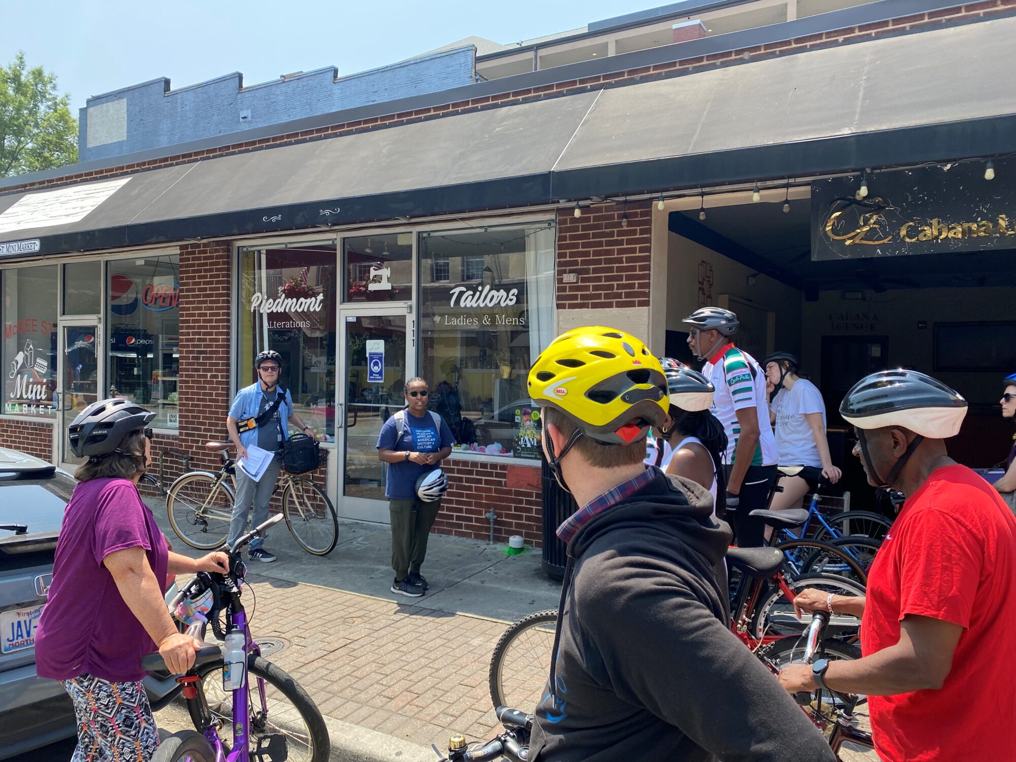 Juneteenth Bike Tour 2023 with cyclists in helmets looking at tour guide in front of a small downtown store
