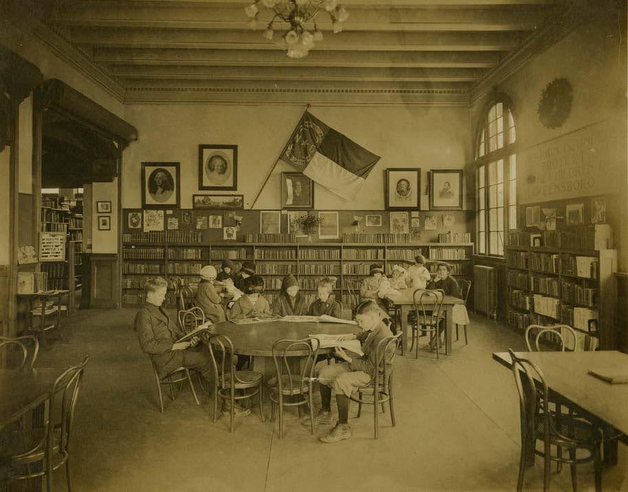 Historic photo of young people people sitting around a library table reading in the 1910s
