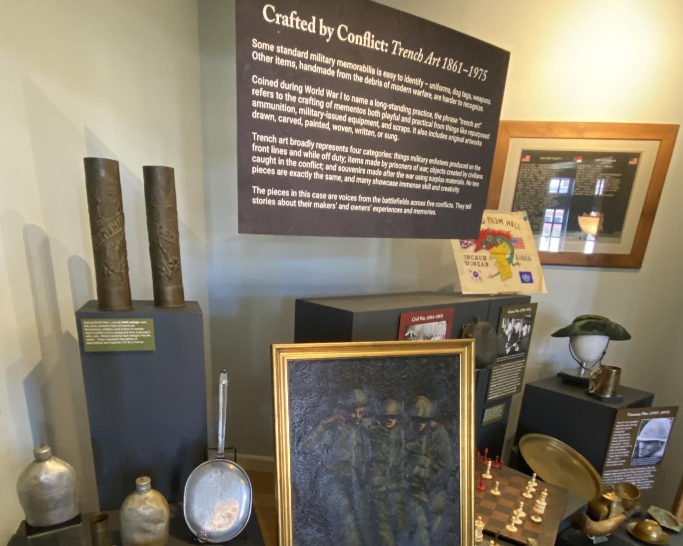 Exhibit case showing Korean War flag, oil painting of three soldiers, etched artillery shells and more